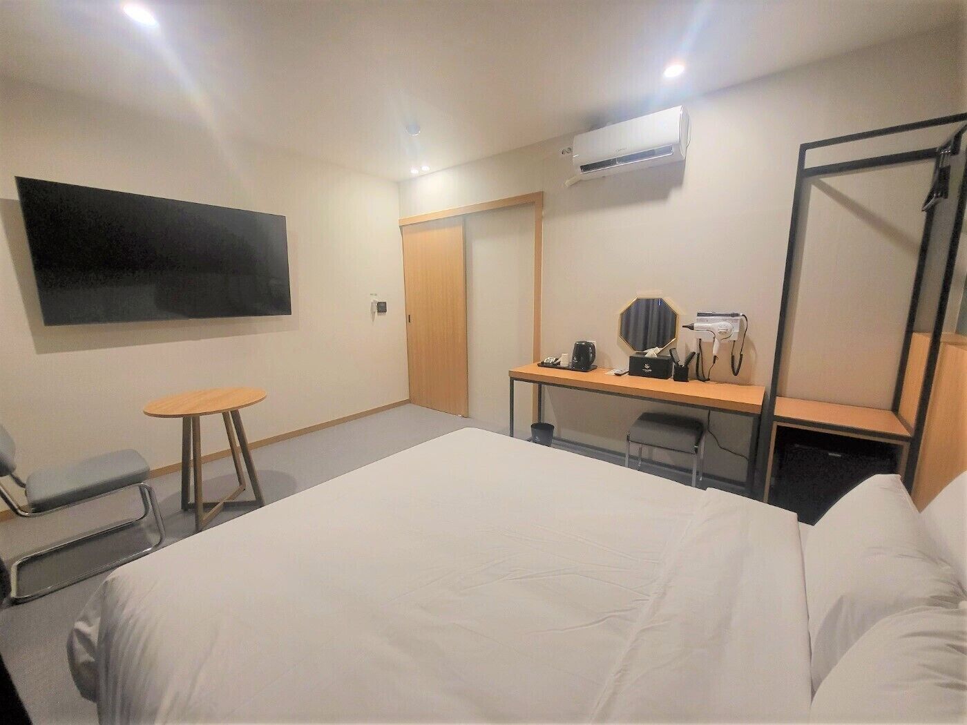 Quarto de hotel com cama, secretária com cadeira, televisão na parede e aparelho de ar condicionado.