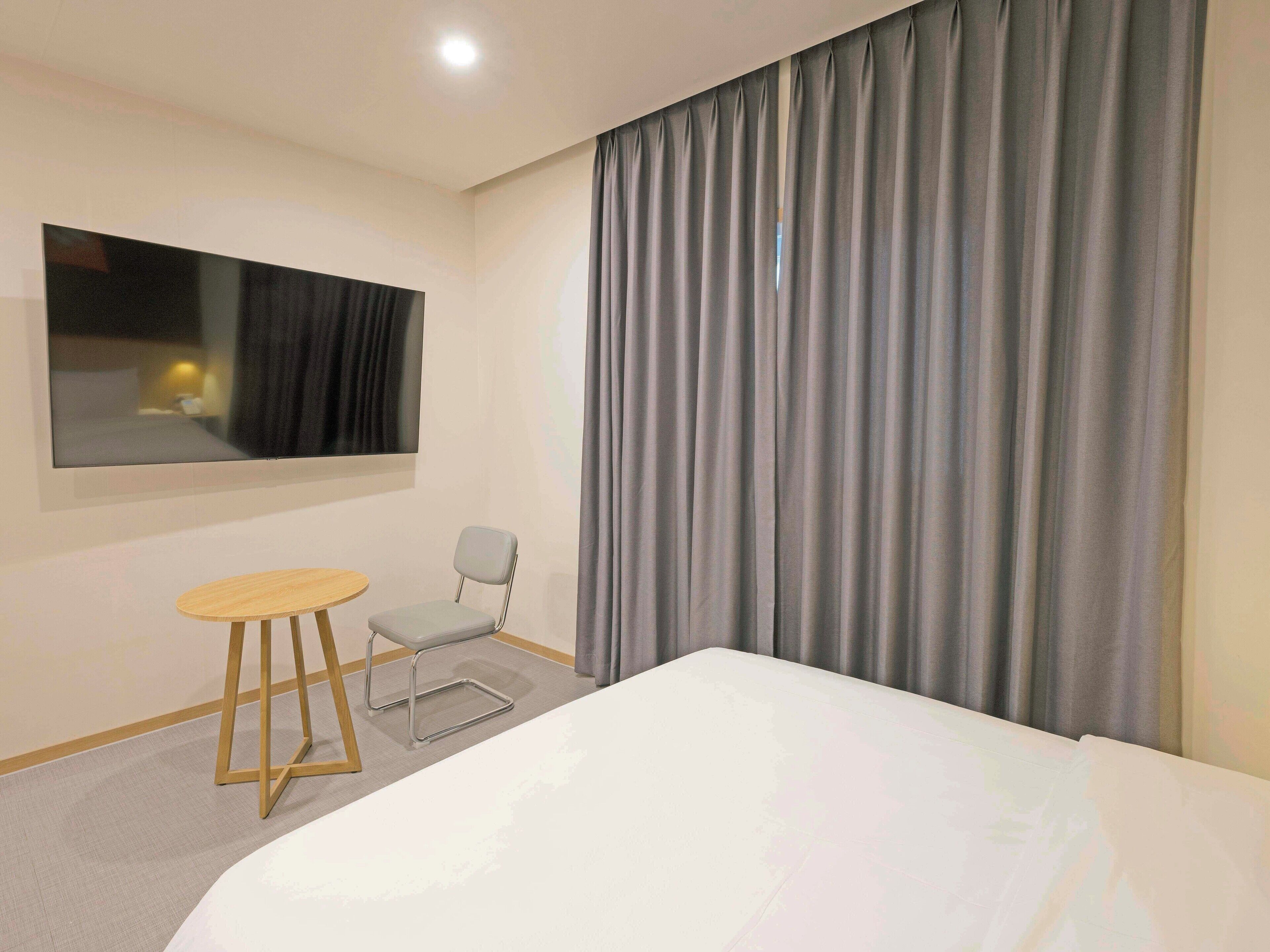 A hotel room with a bed, a small table, a chair, a large mirror, and a window with curtains.