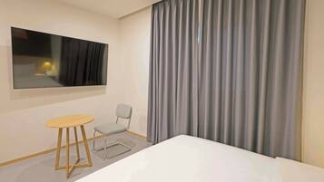 A hotel room with a bed, a small table, a chair, a large mirror, and a window with curtains.