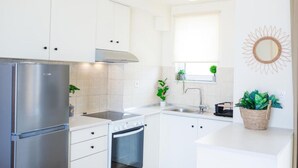 Uma cozinha moderna com armários brancos, eletrodomésticos de aço inoxidável, uma janela com uma planta e um espelho decorativo em formato de sol.