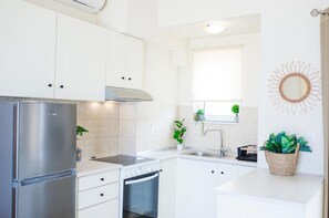 A modern kitchen with white cabinets, stainless steel appliances, a window with a plant, and a decorative sun mirror.