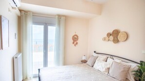 Quarto com cama, mesa de cabeceira, um sonho-apanhador pendurado na parede e vista para o exterior através de uma porta deslizante.