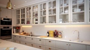 A kitchen with white cabinets, a countertop, and a sink. There are cabinets above the countertop with glass doors containing dishes and kitchen items. - Beautiful 4-bed Flat in Mayfair (London)