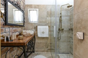 Un baño con pared de piedra, tocador de madera, espejo, perchero para toallas y ducha con cerramiento de vidrio.