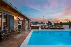 Una piscina con sillas de descanso y sombrillas, un jacuzzi y un patio con vistas a las montañas.