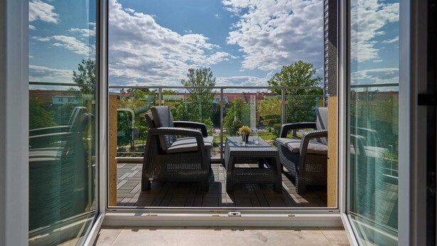 A balcony with wicker furniture and a clear view of the sky and surrounding buildings. - Comfortable Apartment with Parking | Balcony | Air Conditioning (Wroclaw)
