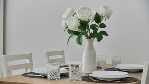 A dining table with white chairs, a white vase with white flowers, and clear glassware. - Comfortable Apartment with Parking | Balcony | Air Conditioning (Wroclaw)
