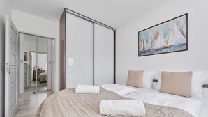 A hotel room with a bed, a painting, a sliding door, and a view into another room. - Comfortable Apartment with Parking | Balcony | Air Conditioning (Wroclaw)