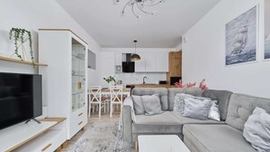 A modern living room with a grey sofa, a flat-screen TV, a dining area, and a kitchen in the background. - Comfortable Apartment with Parking | Balcony | Air Conditioning (Wroclaw)