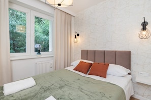 Une chambre à coucher avec un grand lit, une fenêtre avec des rideaux, un radiateur et un luminaire fixé au mur.