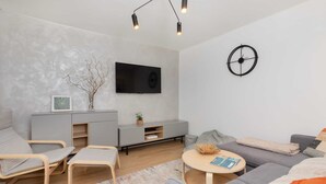 Una sala de estar moderna con un sofá gris, dos sillones, una mesa de centro, un televisor montado en la pared y un reloj.