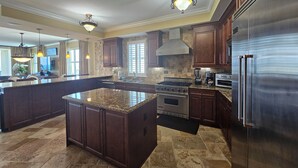 A spacious kitchen with dark wood cabinets, granite countertops, stainless steel appliances, and a large island. - Bella Riva 409 4 bedroom Beachfront (Fort Walton Beach)