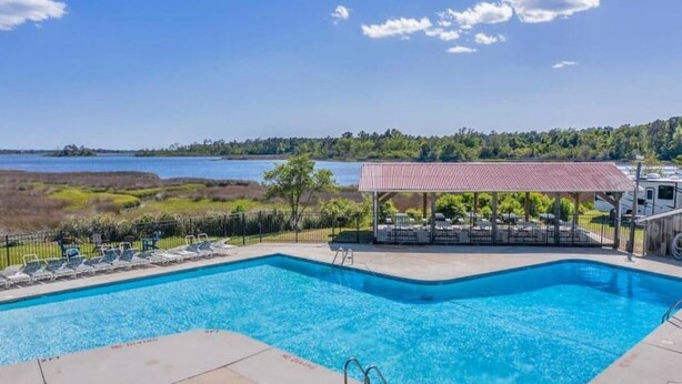 A swimming pool with lounge chairs and a covered seating area, overlooking a body of water. - Family + Pet-Friendly Cabin w/ Loft | Surf City (Holly Ridge)