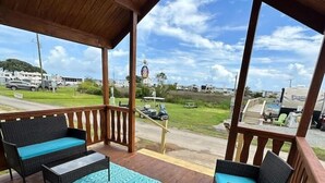 A covered outdoor seating area with wicker furniture and a patterned rug, overlooking a grassy area with RVs and a clear sky. - Family + Pet-Friendly Cabin w/ Loft | Surf City (Holly Ridge)