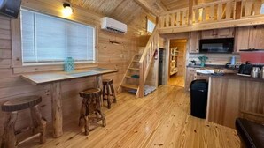 A wooden cabin interior with a kitchen, dining area, and a staircase leading to a loft. - Family + Pet-Friendly Cabin w/ Loft | Surf City (Holly Ridge)