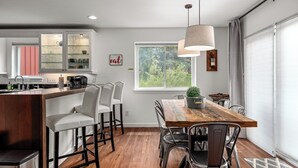 A modern kitchen with a wooden island, bar stools, and a dining table with chairs. - Cozy Creek! End Unit with Creekside Patio, Grill, Top Deck & Communal Hot Tub! (Steamboat Springs)