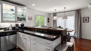 A modern kitchen with a central island, white cabinetry, and a glass-fronted display cabinet. - Cozy Creek! End Unit with Creekside Patio, Grill, Top Deck & Communal Hot Tub! (Steamboat Springs)