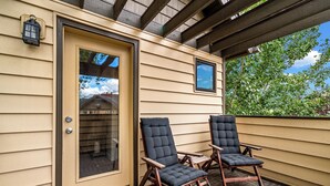 A covered porch with two wooden chairs and a door with a window. - Cozy Creek! End Unit with Creekside Patio, Grill, Top Deck & Communal Hot Tub! (Steamboat Springs)