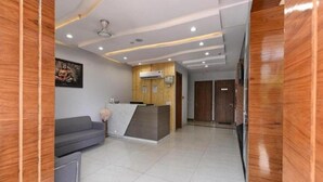 A reception area with a wooden reception desk, a grey sofa, and a tiled floor. - Hotel The Emporio A Corporate suites (Ghaziabad)