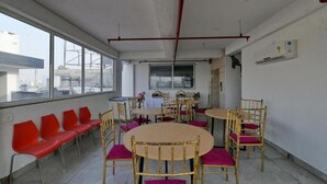 A conference room with round tables and chairs, a large window, and a view of the outside. - Hotel The Emporio A Corporate suites (Ghaziabad)