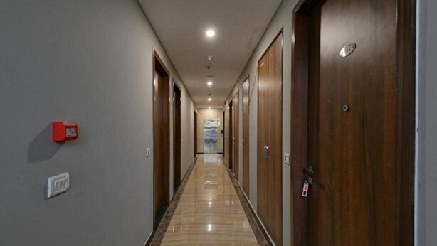 A long, narrow hallway with wooden doors on one side and a marble floor. - Hotel The Emporio A Corporate suites (Ghaziabad)
