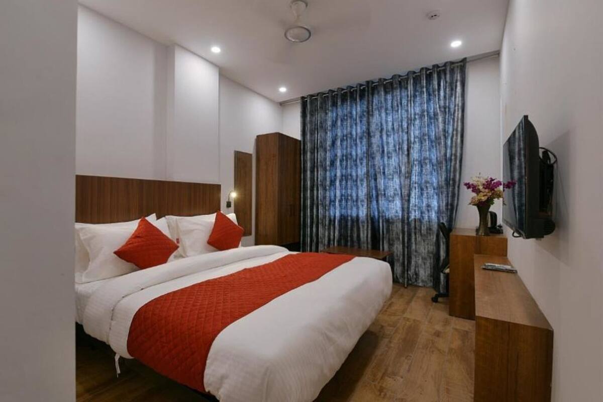 Ein modernes Hotelzimmer mit einem großen Bett, einem hölzernen Kopfteil und einem flachbildfernseher an der Wand.