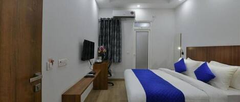 A hotel room with a bed, a desk, a TV, and a door.