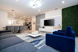 Una sala de estar moderna con un sofá, sillones, una mesa de centro, un televisor y una pared verde.