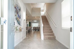 A hallway with a staircase, a dining area with chairs and a table, and a decorative wall piece. - Sleeps 20! Windsor Island 7BR w/ Pool, Gym & Games (Davenport)