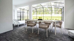 Eine überdachte Terrasse mit Tisch und Stühlen, großen Fenstern und Blick ins Grüne.