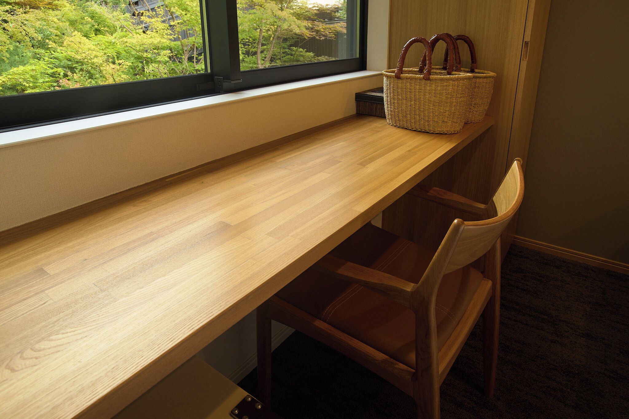 Un bureau en bois, une chaise, un panier et une fenêtre donnant sur un paysage verdoyant.
