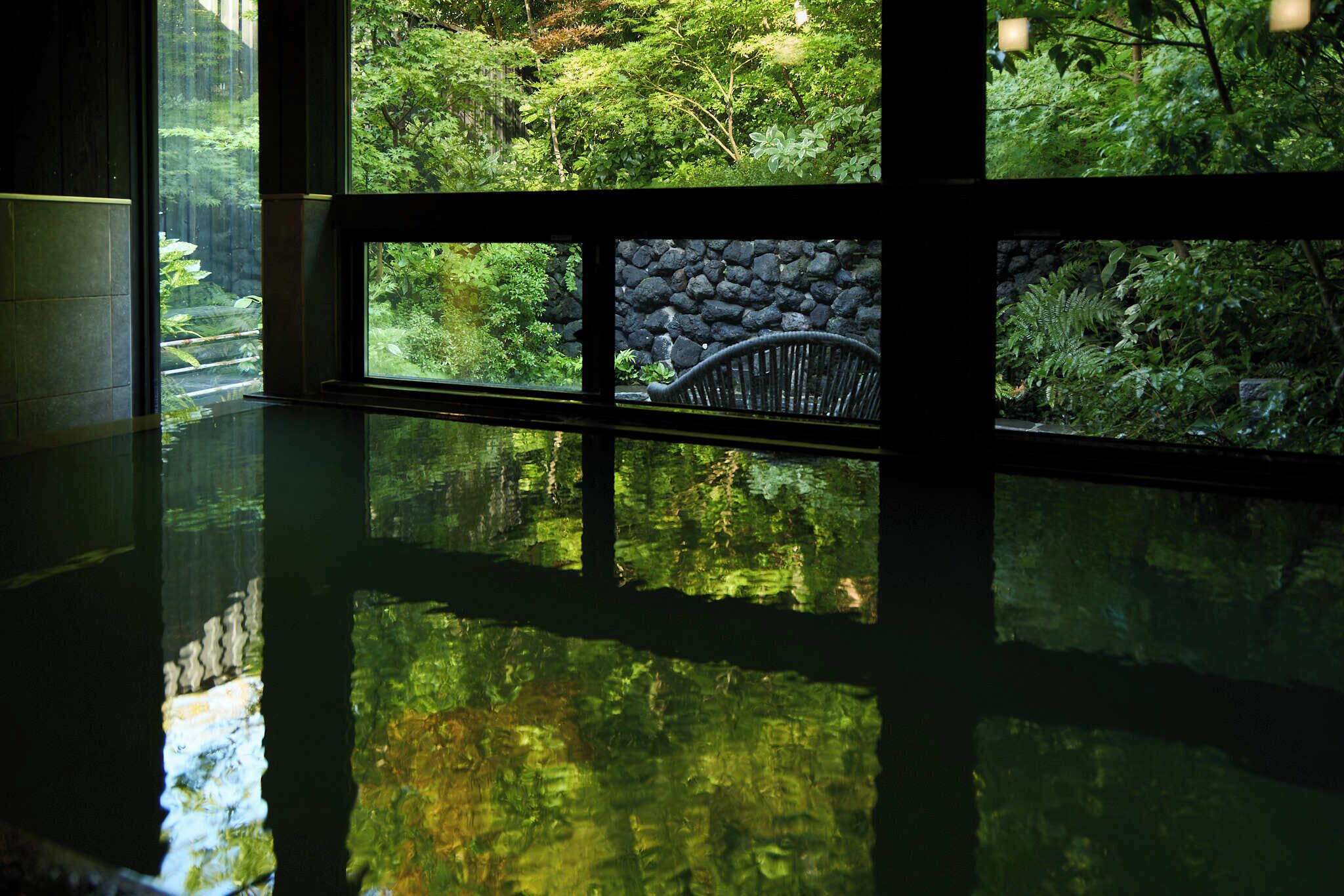 A room with a large window, a stone wall, and a chair.