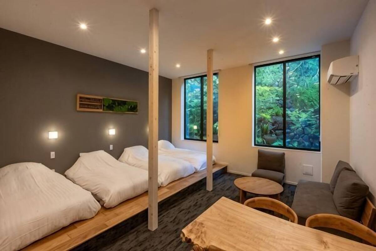 Ein modernes Hotelzimmer mit zwei Betten, einer kleinen Sitzecke und großen Fenstern mit Blick auf einen Wald.