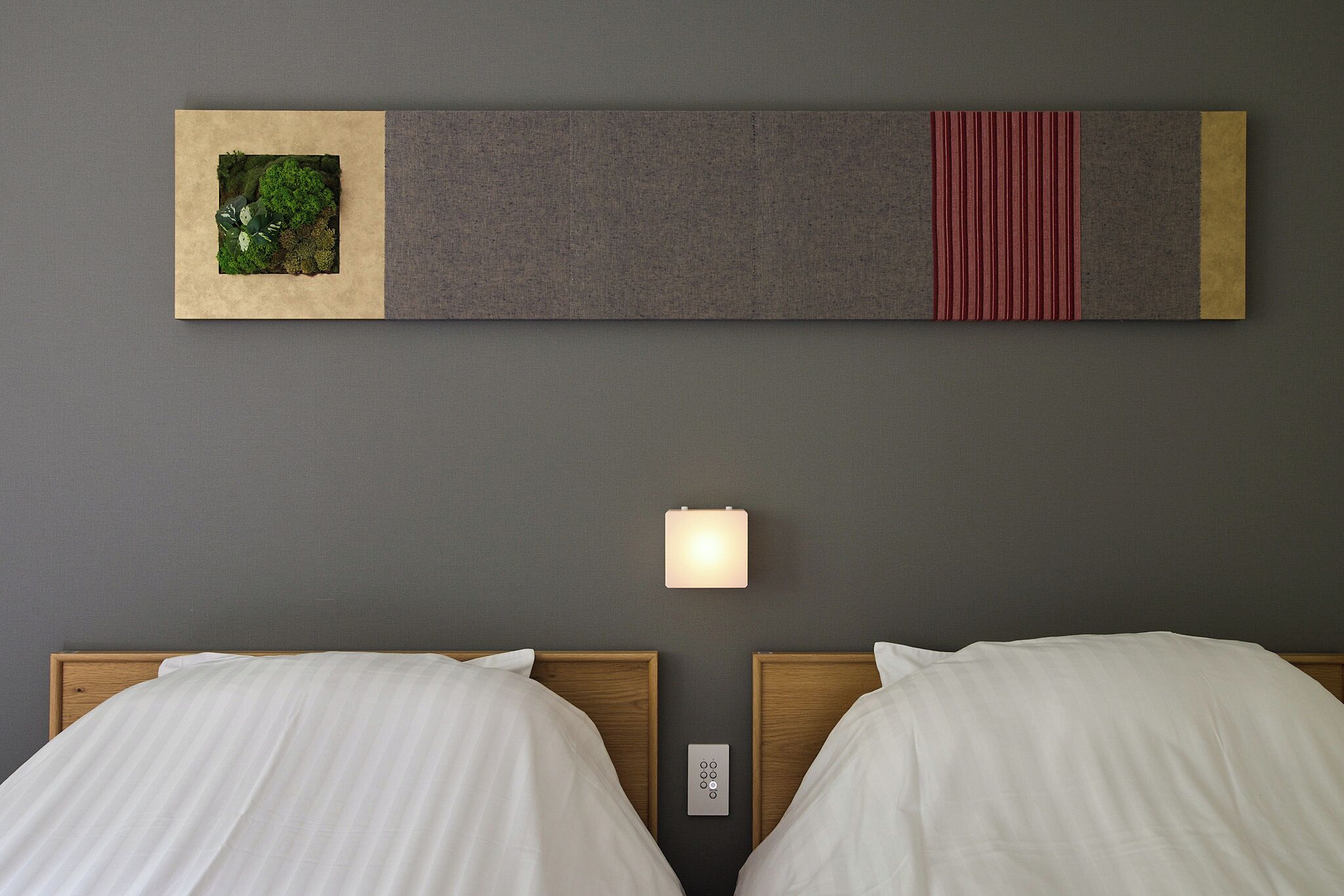 A hotel room with two beds, a wall-mounted light, and a decorative panel above the beds.