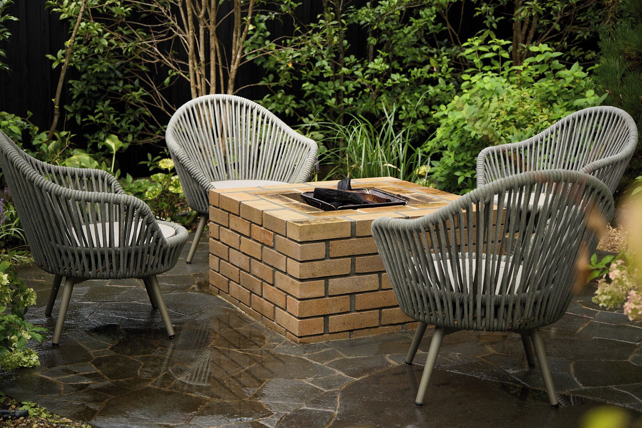 A brick outdoor seating area with four wicker chairs and a table.