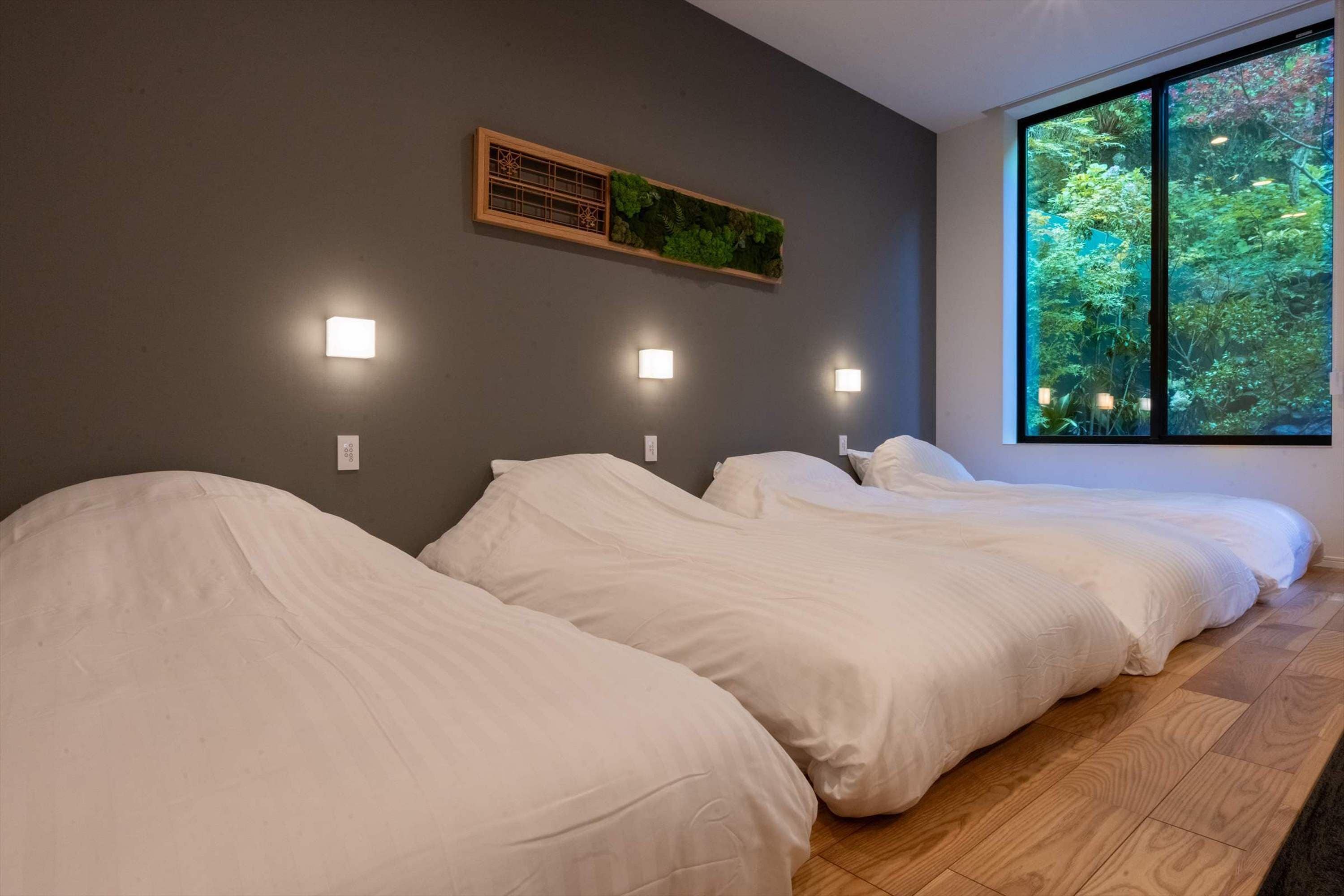 Een hotelkamer met drie bedden, een raam met uitzicht op groen en wandlampen.