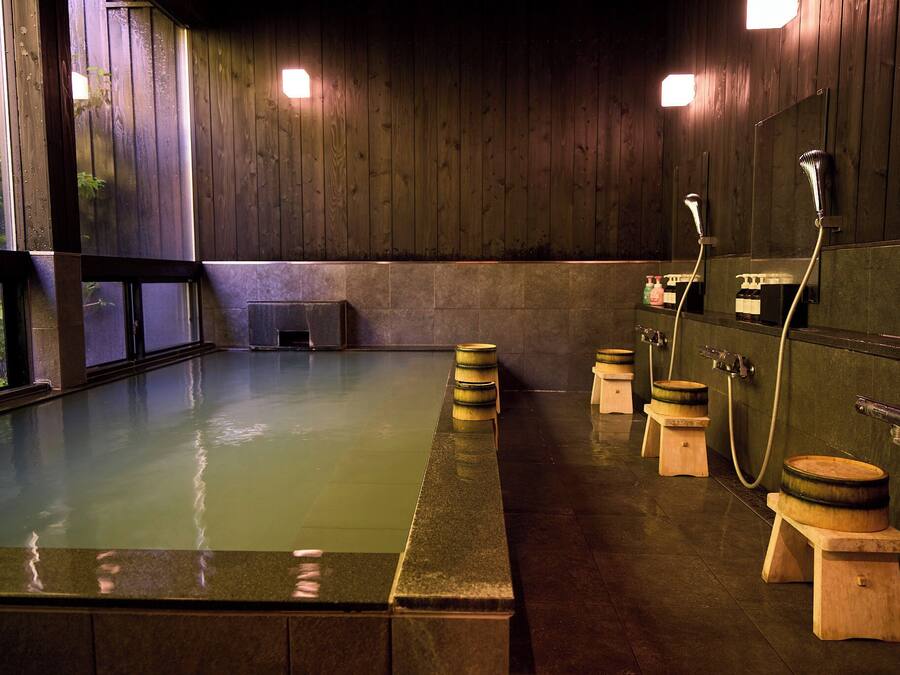 Un onsen japonés tradicional con bancos de madera y una bañera de piedra.