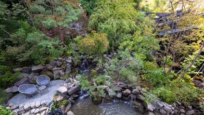 A garden with a small waterfall, stone seating, and lush greenery. - besshoonsen midoriya (Ueda)