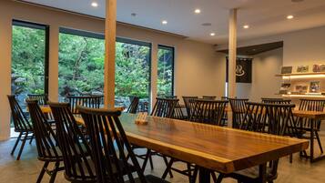 Un restaurante con una larga mesa de madera y sillas negras, amplias ventanas con vistas a zonas verdes y un diseño de interiores moderno.