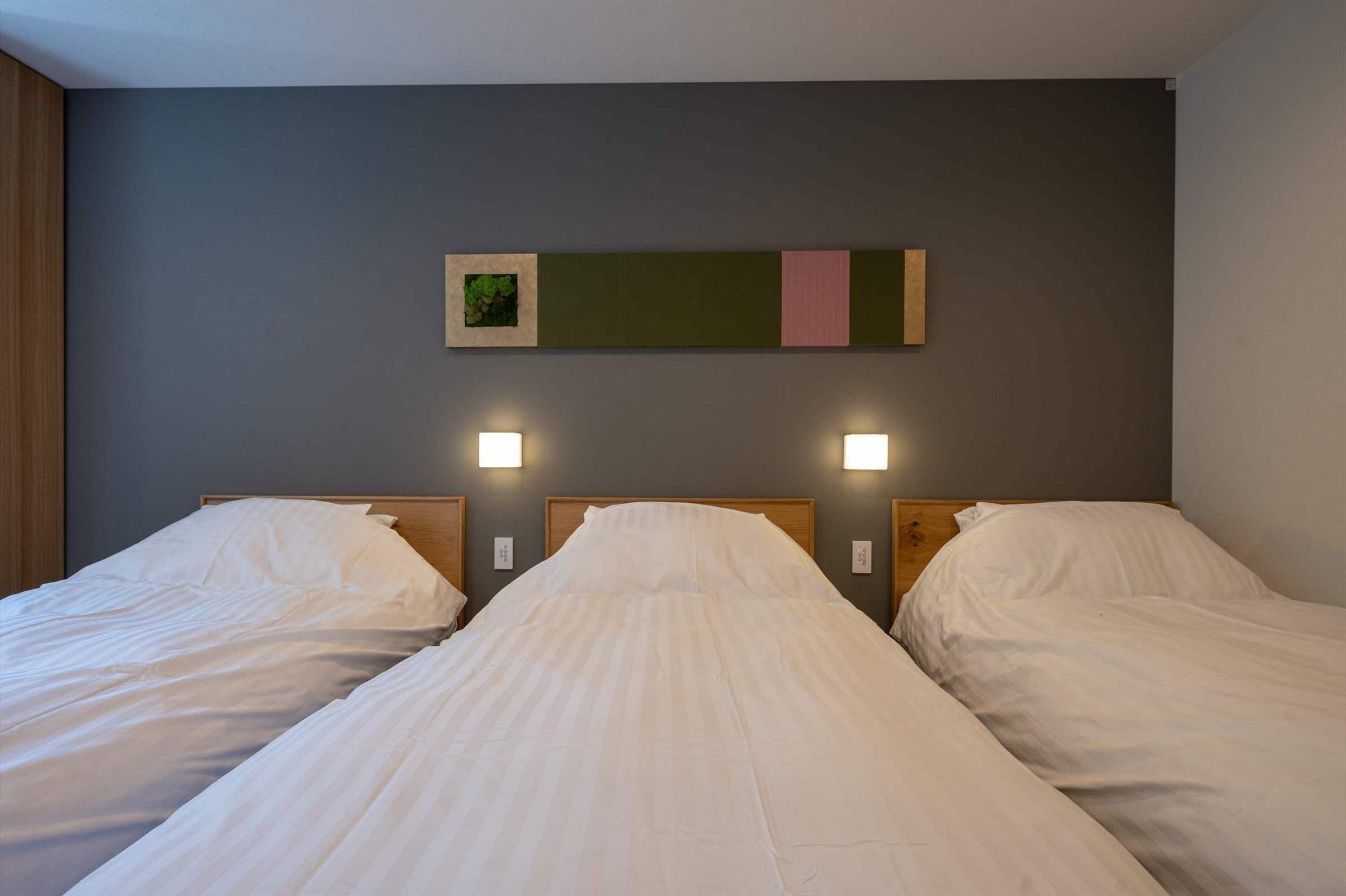 Una habitación de hotel con dos camas, cada una con ropa de cama blanca y cabeceros de madera. Hay luces fijadas en la pared a ambos lados de las camas.