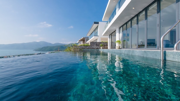 Un bâtiment moderne doté d’une piscine à débordement d’un bleu éclatant, offrant une vue sur une étendue d’eau et sur des montagnes lointaines.