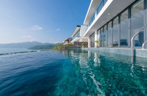 A modern building with a clear blue infinity pool overlooking a body of water and distant mountains. - The Ocean Front Villa Nha Trang Abogo (Nha Trang)