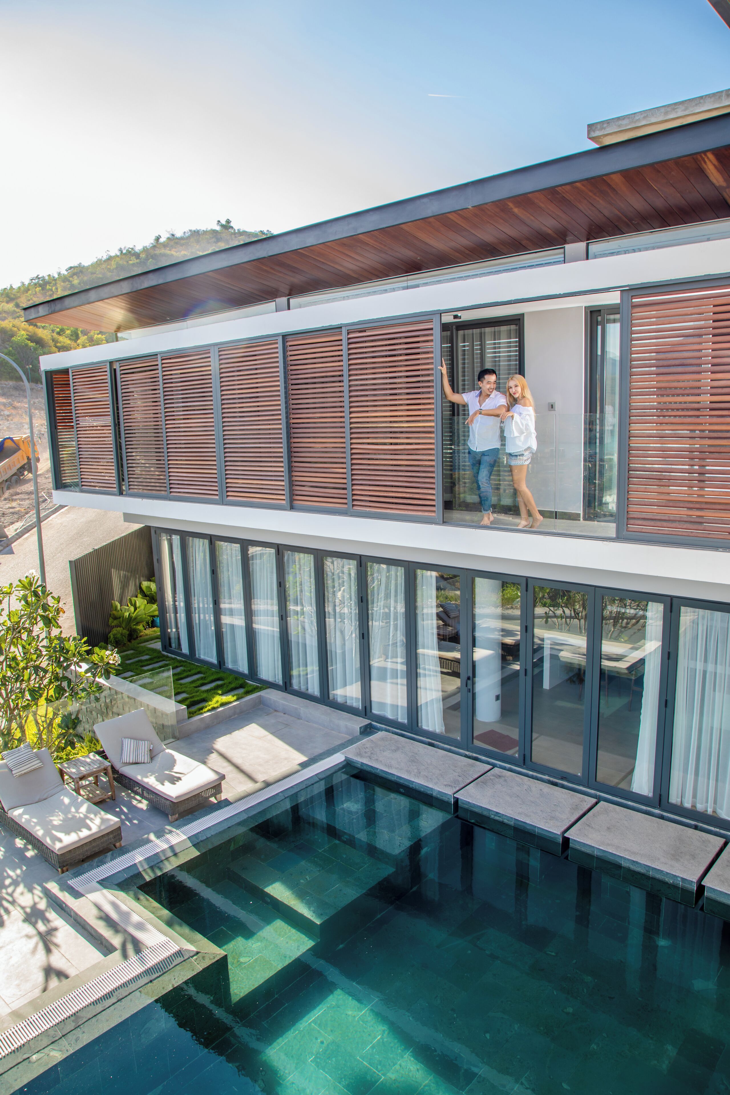 A modern building with a glass balcony, a swimming pool, and outdoor seating.