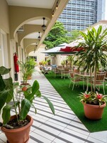 A covered outdoor seating area with tables and chairs, potted plants, and a fire extinguisher on the wall.