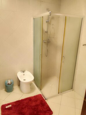 A bathroom with a glass shower enclosure, a white sink, and a red bath mat.