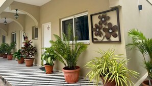 A corridor with potted plants, a framed floral artwork, and a door with a sign. - Natalia Guest House (Luanda)