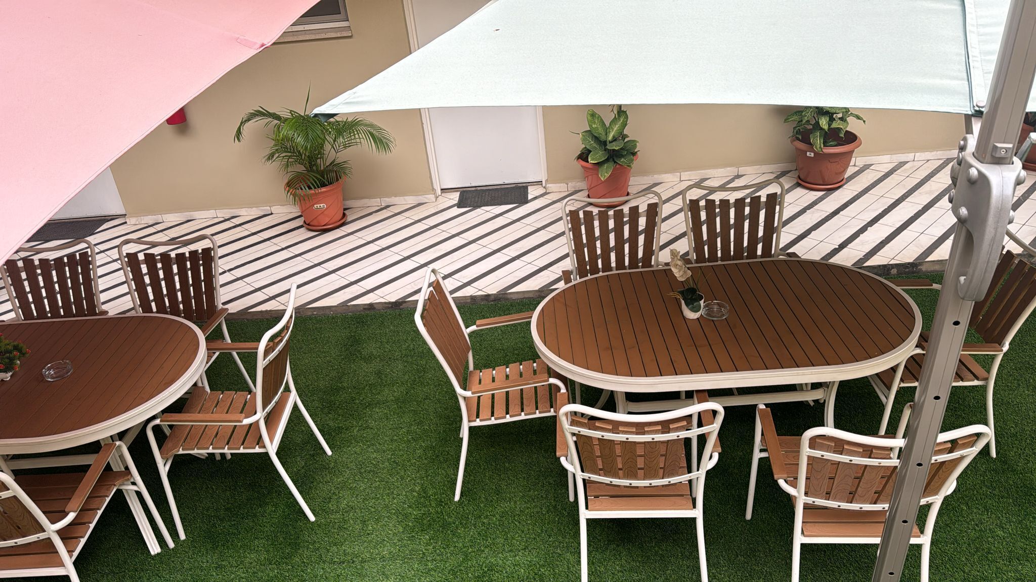 An outdoor patio with a round wooden table and six chairs, surrounded by artificial grass.