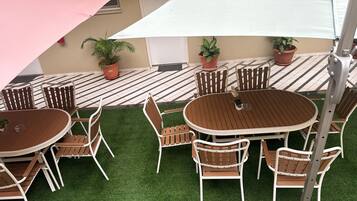 An outdoor patio with a round wooden table and six chairs, surrounded by artificial grass.