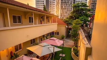 Un pasillo de hotel con varios balcones, zonas de estar al aire libre con sombrillas y una escalera que lleva a un piso superior.