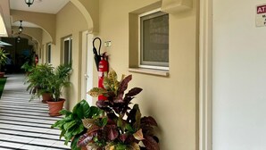 A corridor with potted plants, a fire extinguisher, and a door with an AT sign. - Natalia Guest House (Luanda)